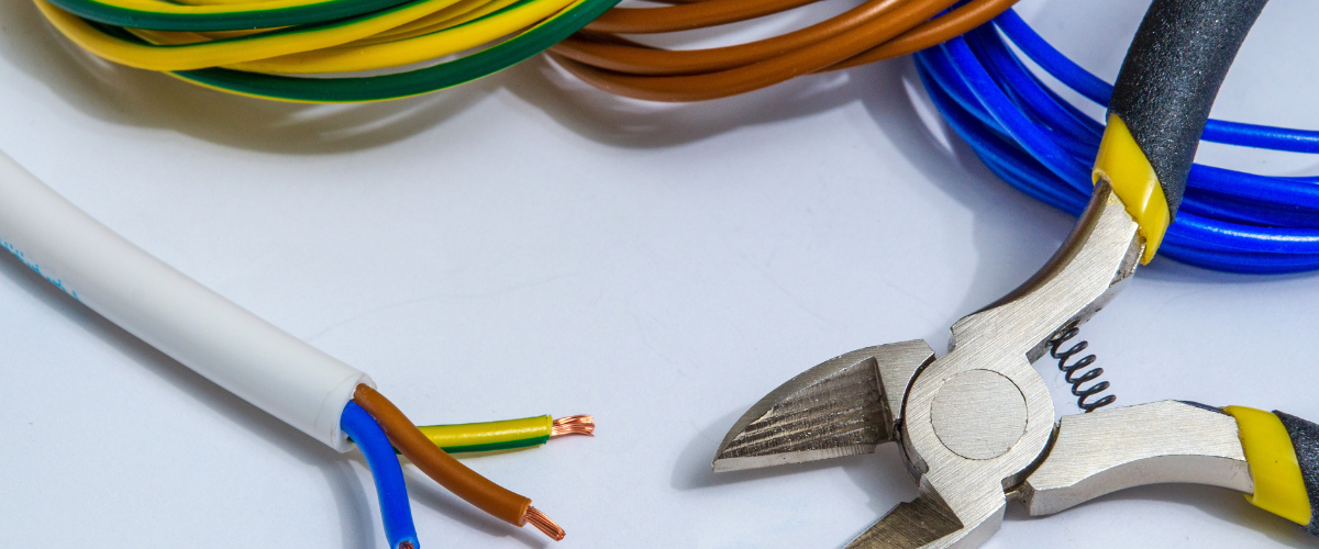 Wire strippers with yellow handles cutting colored electrical wires next to coiled cables in various colors including yellow-green, brown, and blue.