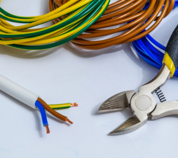 Wire strippers with yellow handles cutting colored electrical wires next to coiled cables in various colors including yellow-green, brown, and blue.